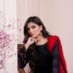 Portrait of a young woman in traditional black attire with red accents, indoors.