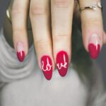 Vibrant red nails with 'love' art on a woman's hand, showcasing elegant style and design.